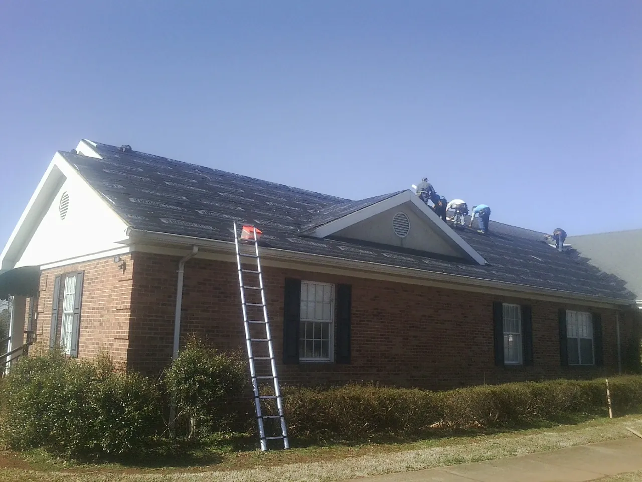 Crew tearing shingles off a brick ranch roof with a ladder set — Emergency Roof Repair work by our crew in Shingle Springs