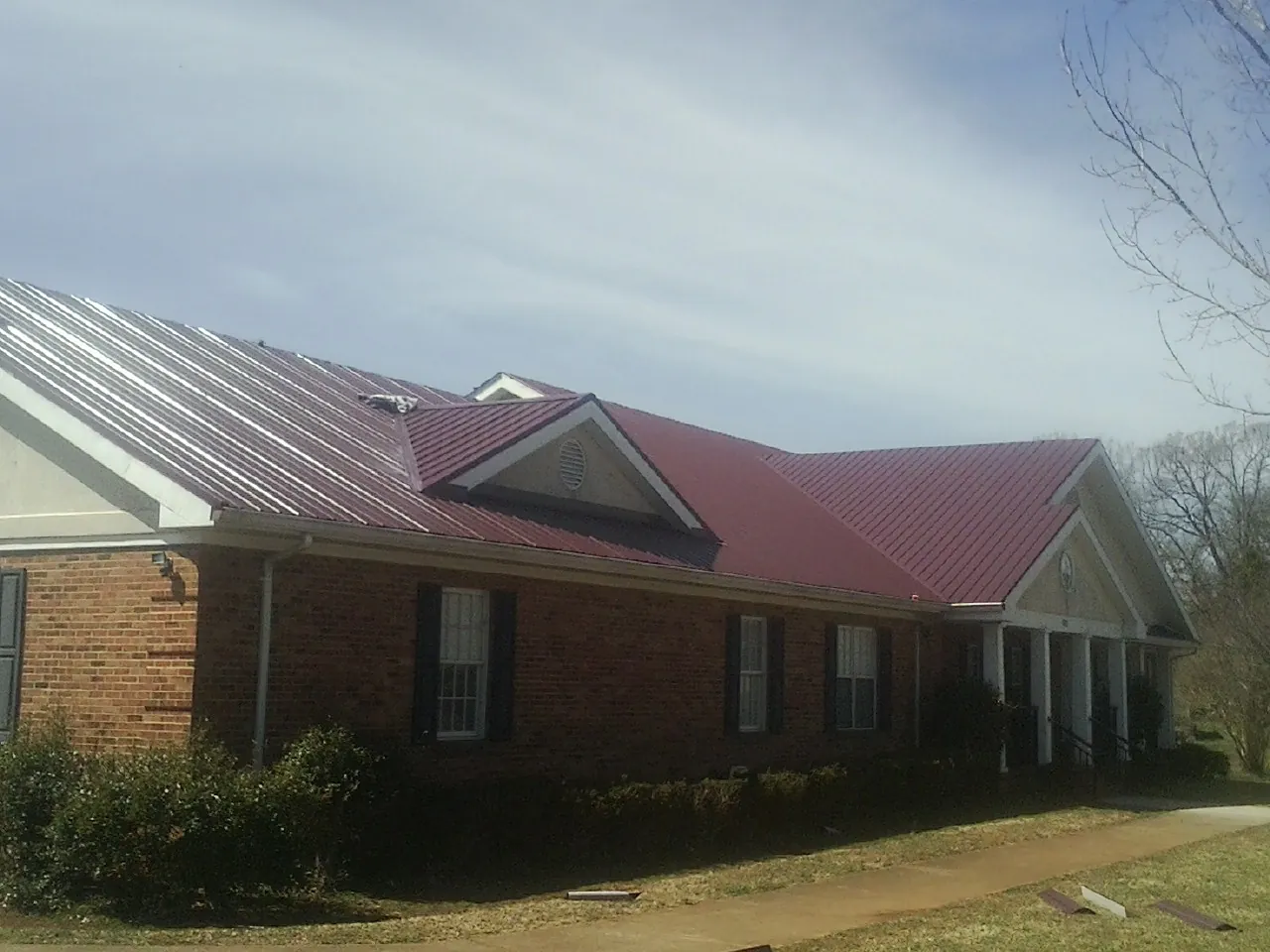Red metal roof with gabled entries on a long brick building, from a Hail Damage Roof Repair job in Shingle Springs