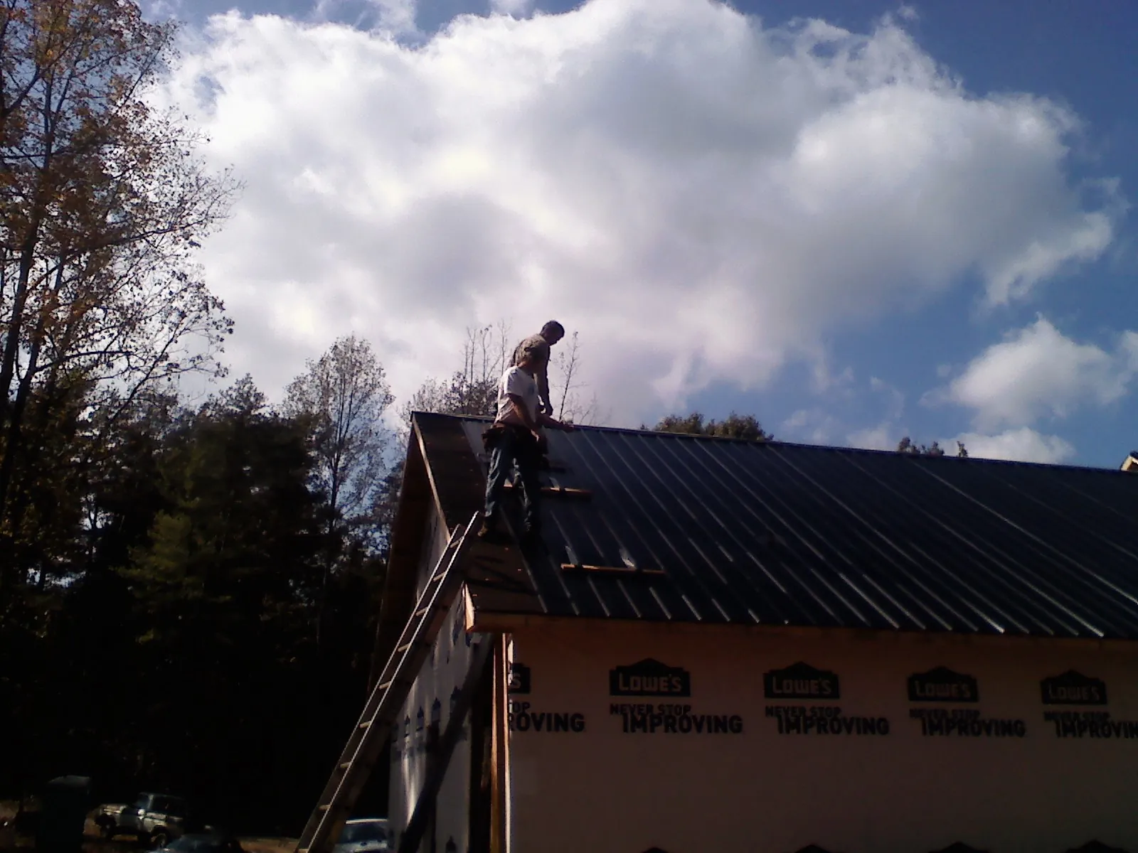 Roofer fastening dark metal panels high against a cloudy sky in Shingle Springs