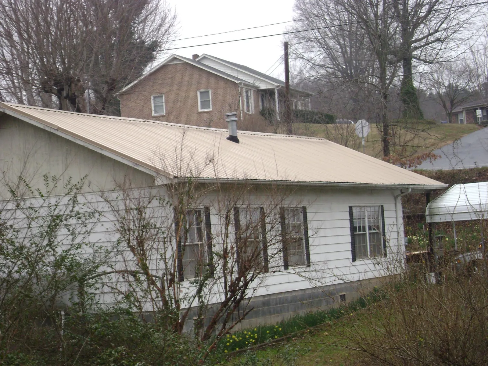 Tan metal roof on a white sided house set into a hillside — Commercial Roofing by Roofing Brothers in Shingle Springs